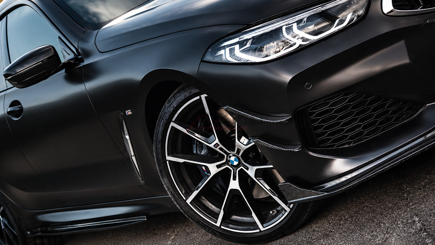 Mattschwarz lackierter BMW 8er mit montierten A8X1 Echtcarbon Front Canards am Frontbereich, Detailaufnahme mit Felge und Scheinwerfer