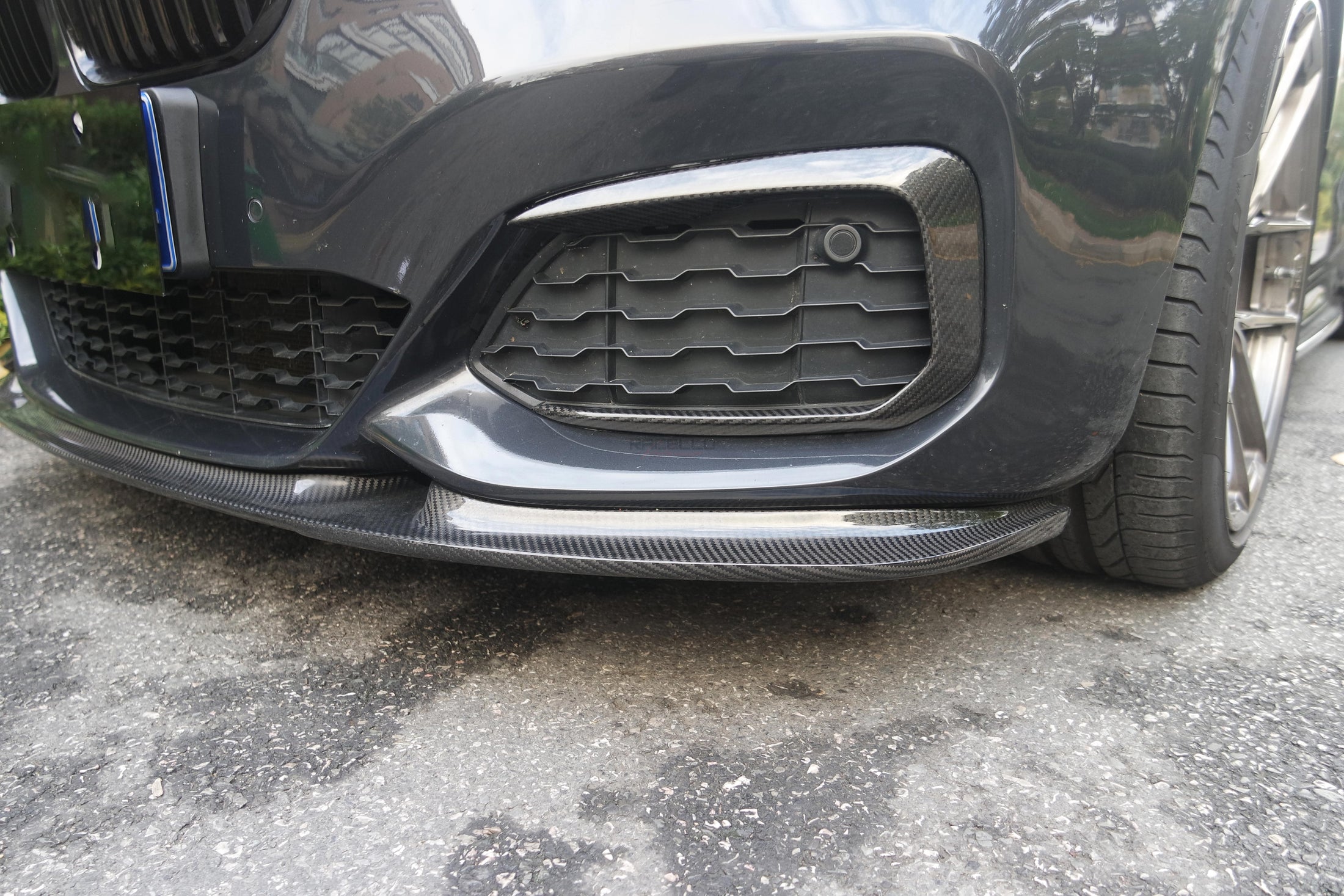 L1X1 Echtcarbon Frontspoiler montiert an der M Sport Frontstoßstange eines dunklen BMW 1er F20 LCI, Nahaufnahme von vorne unten